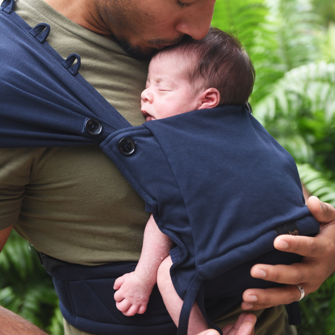 Eltern tragen ihr Neugeborenes in der Neko Tiny Babytrage in Navy – sanft, ergonomisch und anschmiegsam.